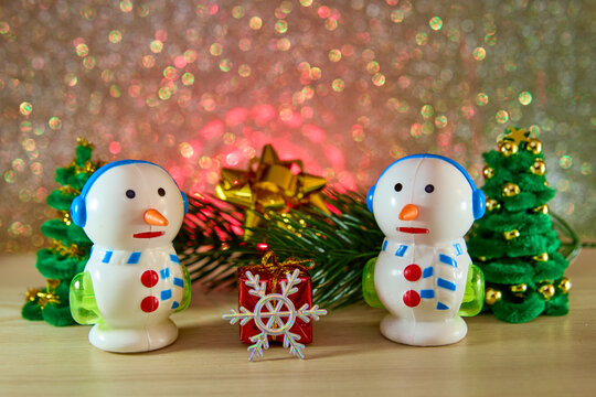 Unusual snowmen and a snowflake with a gift near a Christmas tree branch and fir trees