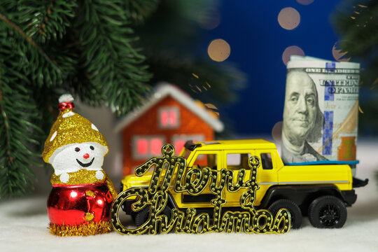 A snowman with letters and a yellow car with dollar bills in the back against the backdrop of an orange house under a Christmas tree