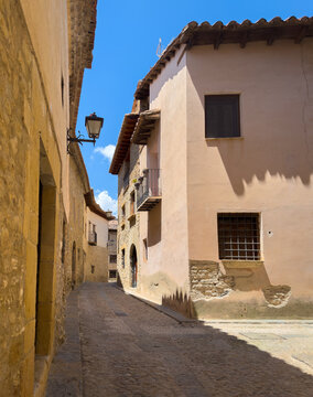 Narrow cobbled alley lined with stone and plastered buildings, wrought-iron balcony, and vintage street lamp in the medieval village of Mirambel, Teruel, Aragon, Spain
