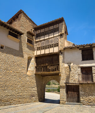 Historic stone archway passage topped by ornate carved wooden gallery with geometric lattice windows and spiral balusters in medieval village of Mirambel, Teruel, Aragon, Spain
