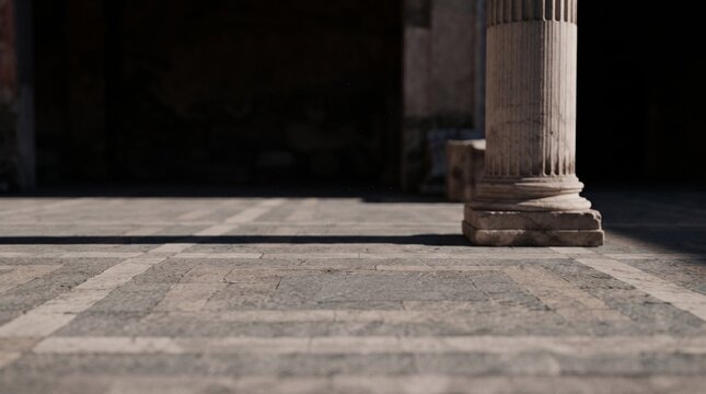 Classical stone column base on a geometric paved floor with deep sunlight shadows