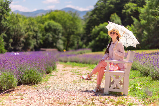 Graceful Caucasian woman sitting on bench in vibrant lavender field during Provence vacation. Natural beauty and elegance define relaxed summer lifestyle.