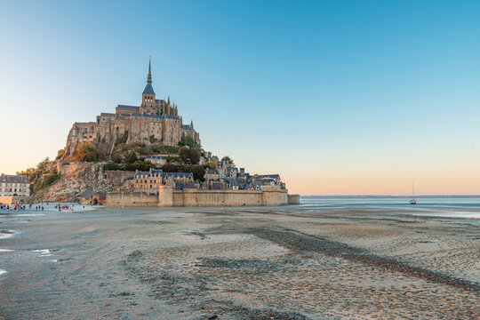 Mont Saint-Michel abbey at low tide under clear blue sky with medieval architecture and scenic coastal landscape at sunset in Normandy, France. Tidal island with monastery in Normandie