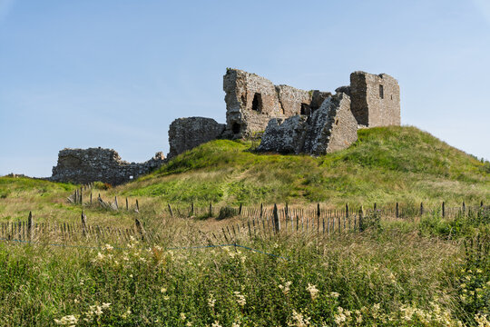 Historic Duffus Castle ruins overlooking green fields under a vibrant July sky in Moray, Scotland
