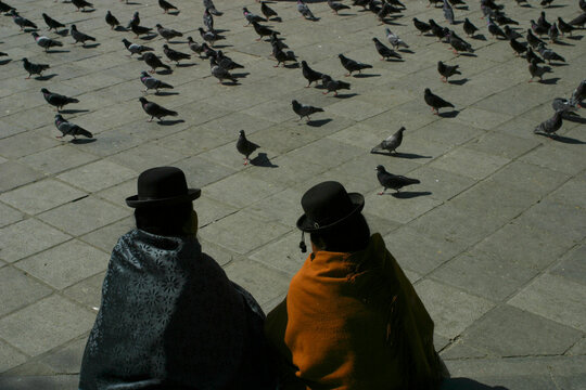 Two Bolivian women sit in a square with lots of pigeons in central La Paz.