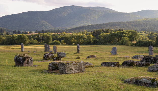 Wide view of a medieval stecci necropolis in a mountain meadow surrounded by forests near Novi Travnik, Bosnia and Herzegovina.