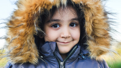 Young child smiling, wearing winter coat with fur hood outdoors, enjoying cold weather © Довидович Михаил