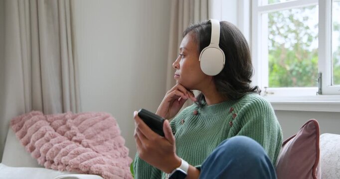 African American adult woman tapping smartphone starting audio, listening with headphones on sofa