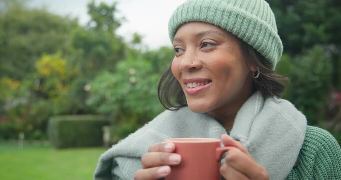 African American woman with beanie sitting in cool yard holding mug inhaling aroma sipping warming