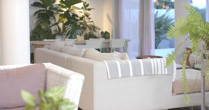 Camera is pulling back, panning right, revealing beige sofa and plants at home, showcasing decor