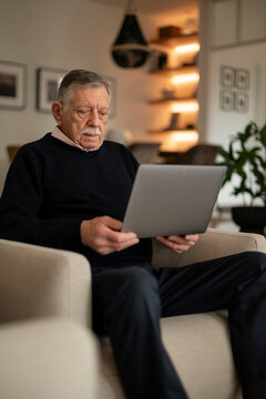 Senior man sitting in armchair and using a laptop at home