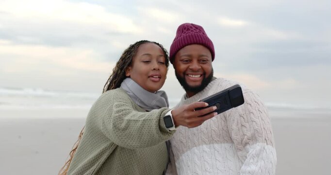 African American couple on beach woman extending phone taking selfies capturing memories in knits