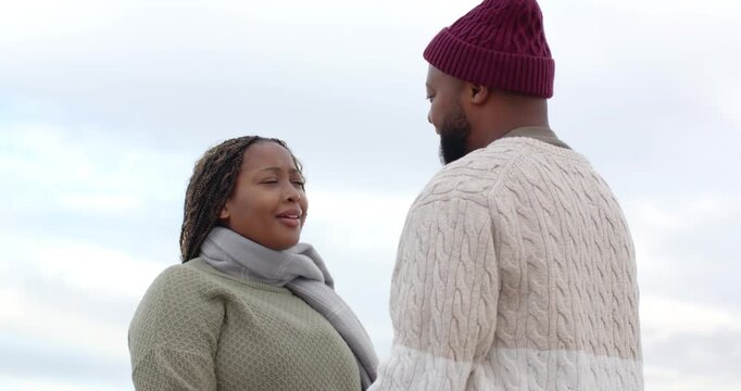 African couple exchanging eye contact touching foreheads showing love wearing beanie under clouds
