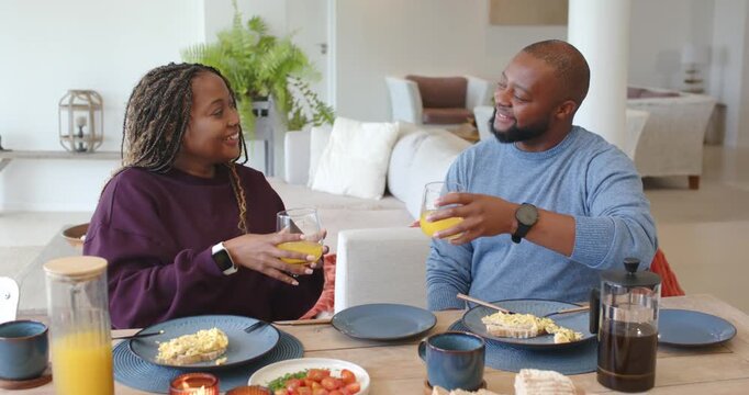 African American couple at breakfast table woman reaching pitcher, pouring juice, toasting
