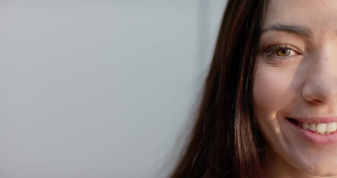 Adult woman reacting to offscreen cue, smiling, laughing, right face at light-gray wall, copy space