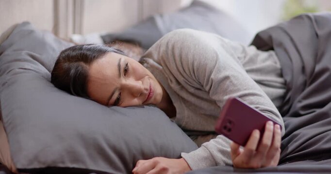 Couple, adult woman lying left in bed holding purple phone reading message after alert appearing