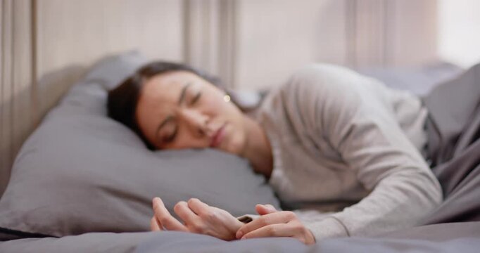 Female wearing gray top lying on bed holding red phone, scrolling, checking forehead for ache