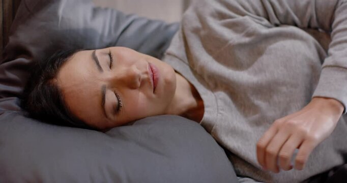 Woman reclining on bed settling and shifting hands in pullover hugging gray pillow for comfort