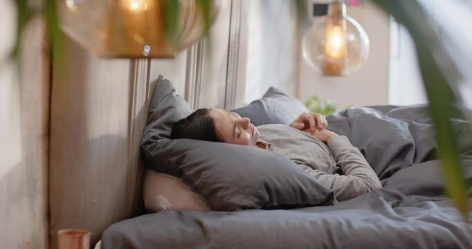 Adult woman in bed after rubbing eyes, turning onto side, adjusting pillow, curling into rest