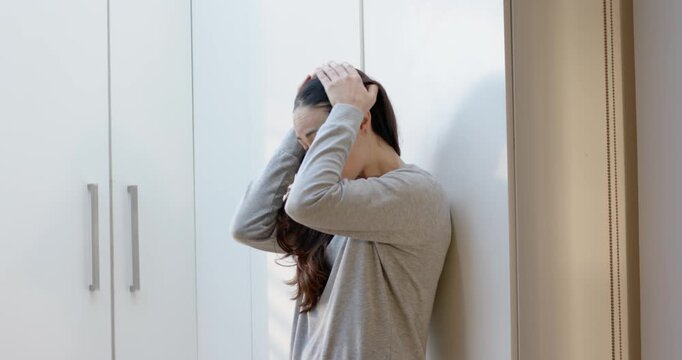 Adult woman covering face, breathing, sitting in pjs by white cabinets, calming down, copy space