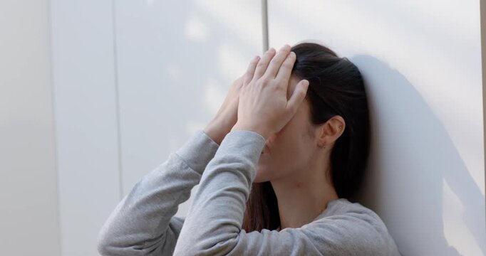 Adult female grey top pajamas rubbing eyes holding face resting on white paneled wall, copy space
