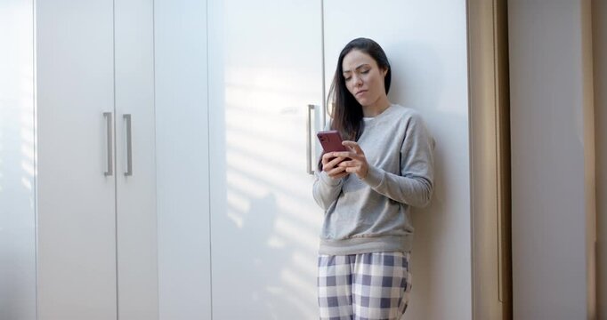 Woman gray sweatshirt reading pink-phone lowering reaching slim handle wardrobe checking right side