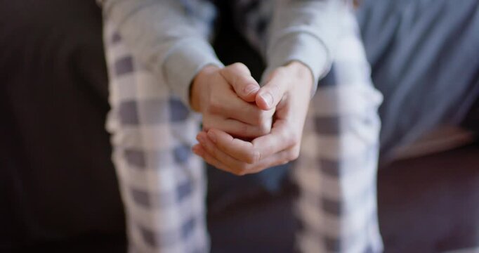 Female fidgeting hands on couch after loose clasp in plaid pants and sweatshirt, relieving stress