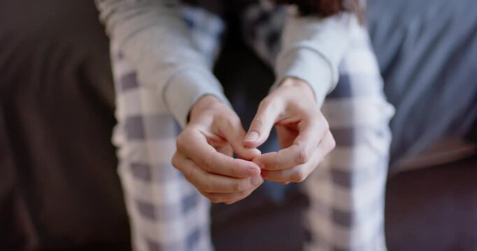 Adult female sitting on bed in plaid pants, pensive, picking nail while camera pulling back