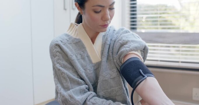 Asian woman on ottoman looking at left arm rolling sleeve securing cuff linking monitor checking BP