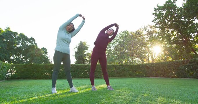 African American female friends mirroring side bends on lawn at sunrise in activewear and sneakers