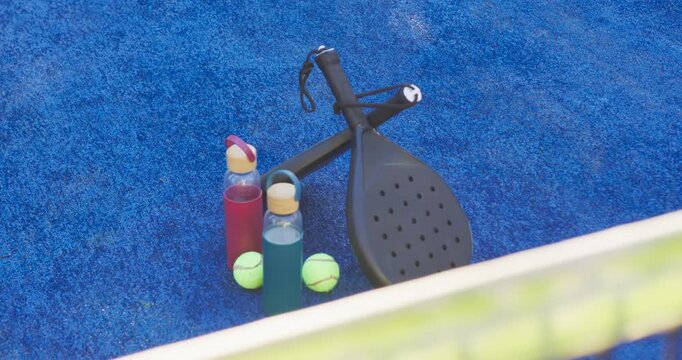 Camera is pulling in, revealing paddles, bottles and balls on blue court to show detail