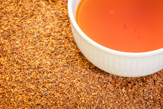 rooibos red tea  -  a white cup of a hot drink and loose leaves on grunge wood background, tea made from the South African red bush, naturally caffeine free