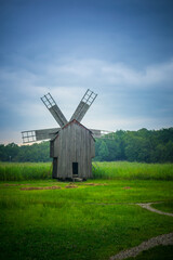 Obraz premium Rustic wooden windmill stands in a lush green field under a cloudy sky.