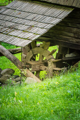 Rustic wooden waterwheel by a grassy hillside in a serene countryside setting. © Letitia