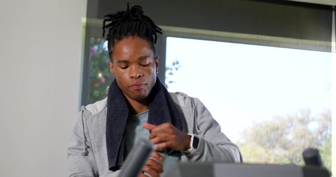 Adult African American man leaning, twisting water bottle cap, sipping, hydrating on treadmill