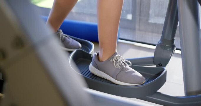 Man pushing right pedal, alternating feet on elliptical trainer for cardio workout by window