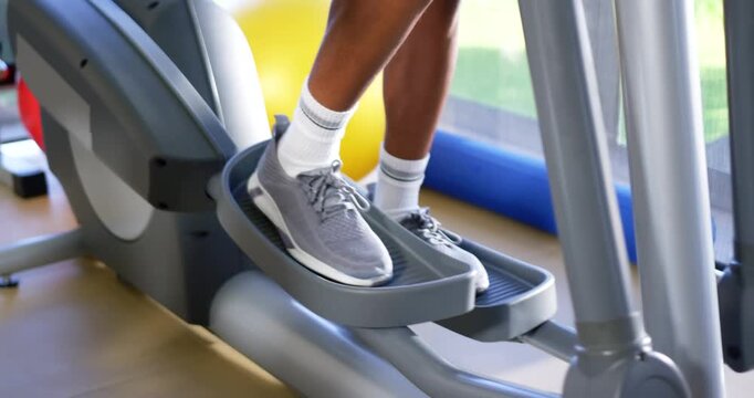 Adult male starting exercise by planting feet on elliptical pedals, alternating stride near window