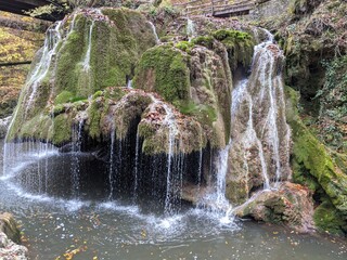 Picturesque waterfall cascades over lush green moss-covered rocks in a serene forest setting. © Letitia