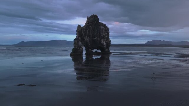 Cinematic aerial drone footage of the iconic Hv&iacute;tserkur sea stack rising from the North Atlantic Ocean during sunset in North Iceland. Volcanic basalt rock formation on the shoreline