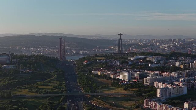 Stunning drone footage capturing multiple cars traveling on busy motorway heading towards Lisbon with Christ the King monument and 25 de Abril bridge landmarks in scenic background

