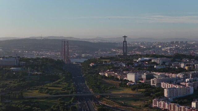 Aerial drone view of heavy traffic on Portuguese highway approaching Lisbon city with Almada skyline, iconic Christ the King statue and 25 de Abril suspension bridge visible in the distance