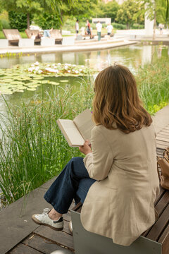 Rear view of a blond haired woman reading a book in a peaceful city park