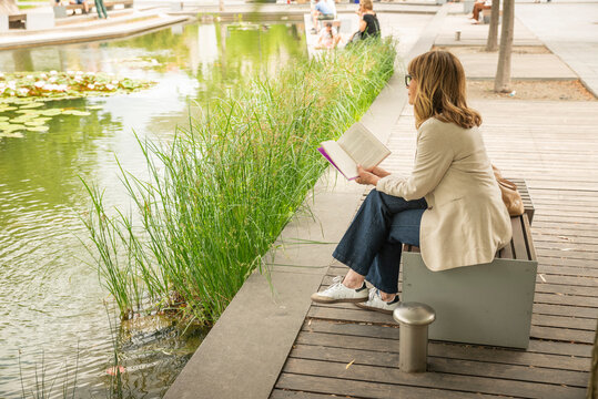 Mature blond haired woman reading a book in a peaceful city park
