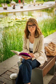 Mature blond haired woman reading a book in a peaceful city park