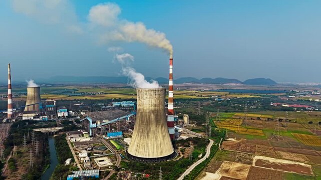 An aerial view of a coal power plant chimney emitting smoke above surrounding fields in Vijayawada, India in 2026