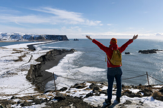 A person standing along a stunning black sandy beach Reynisfjara and rocky terrain in VIK Myrdal in Golden Circle area in Iceland with Atlantic Ocean waves crashing and volcanic rock formations