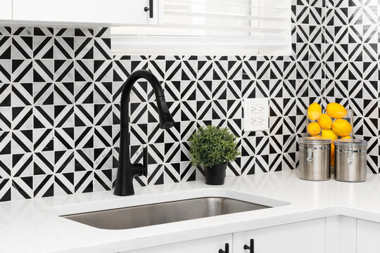 A black kitchen faucet detail with diamond black marquina and carrara white marble tile backsplash, white marble countertop, and white modern cabinets.