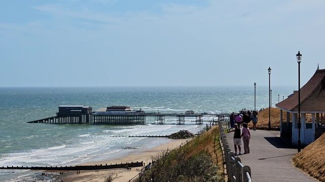 Pull-back shot of Cromer Beach and the clifftop path on the North Norfolk coast, captured on a bright, sunny summer day. Expansive sea views, golden sands, and dramatic cliffs.