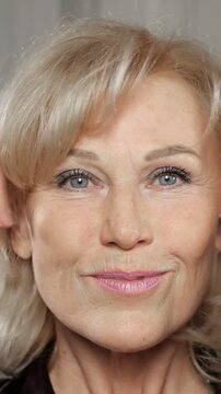 Beautiful senior woman with blonde hair and blue eyes applying cream and massaging her face and neck for an anti aging lifting effect, demonstrating a daily beauty and skincare routine