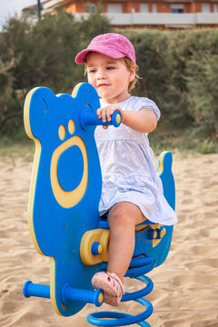 Toddler girl riding playground spring rocker on sandy playground